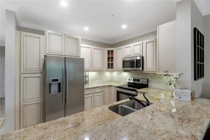 Kitchen with stainless steel appliances, light stone counters, backsplash, glass insert cabinets, and crown molding