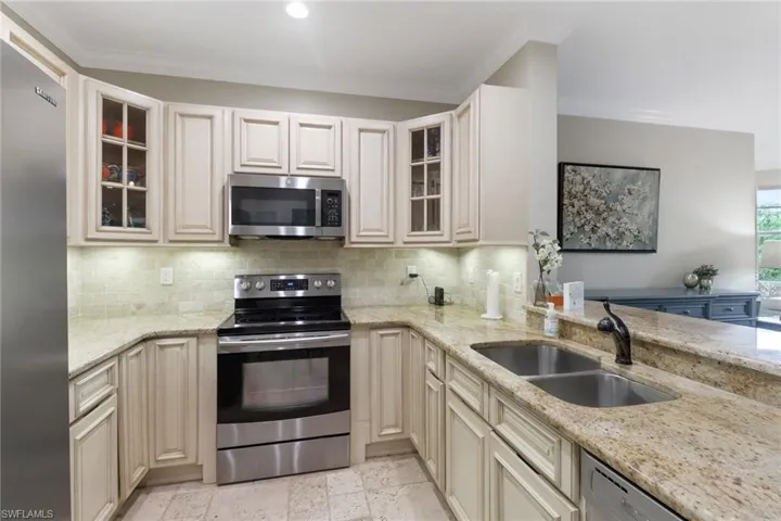 Kitchen featuring stainless steel appliances, backsplash, light stone counters, cream cabinets, and crown molding