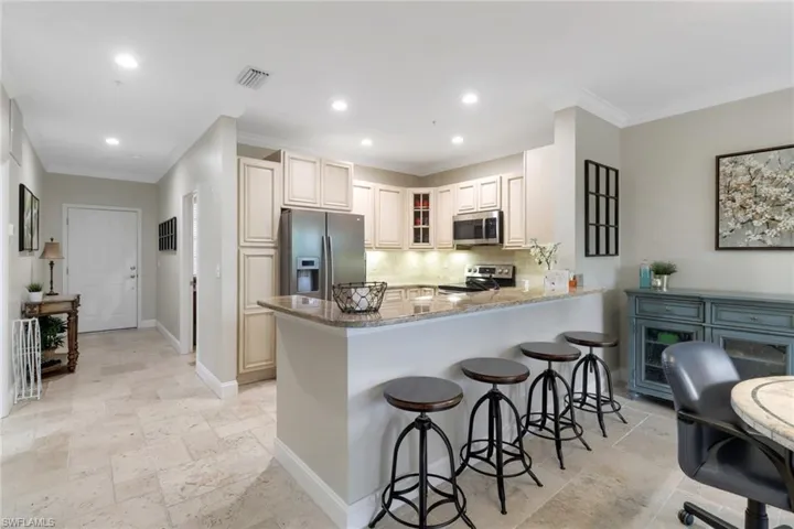 Kitchen featuring appliances with stainless steel finishes, stone tile flooring, a peninsula, decorative backsplash, and a kitchen breakfast bar