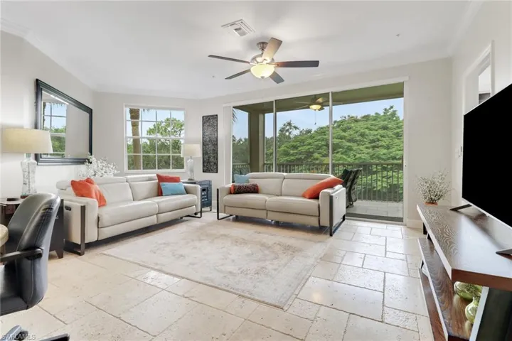 Living room featuring stone tile flooring, crown molding, and a ceiling fan