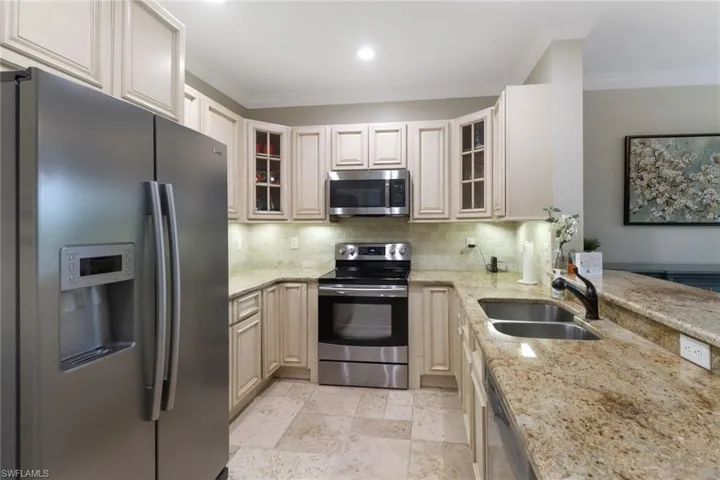 Kitchen featuring stainless steel appliances, tasteful backsplash, crown molding, light stone counters, and glass insert cabinets