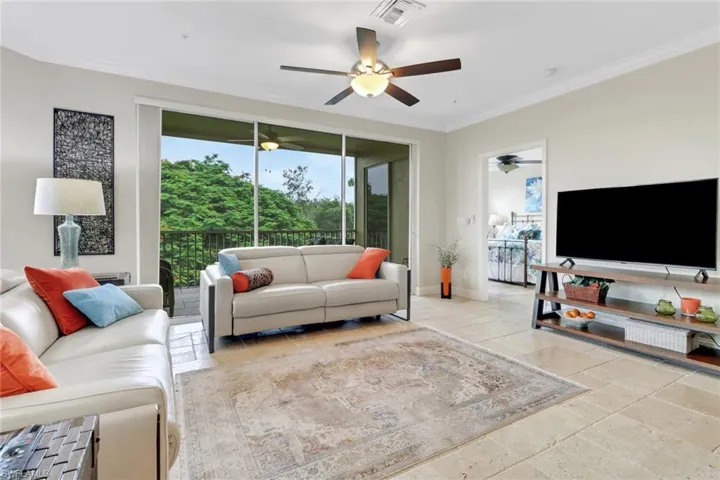 Living room featuring ceiling fan, ornamental molding, and stone tile floors