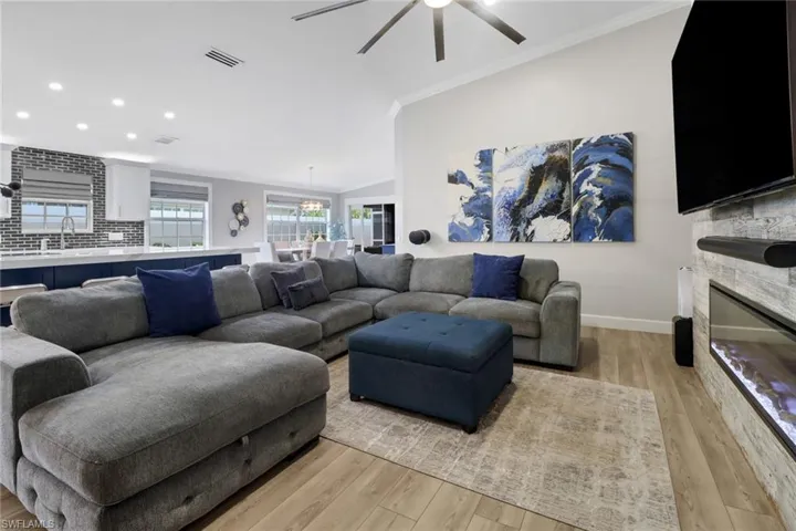Living room featuring crown molding, a stone fireplace, light wood-type flooring, and ceiling fan
