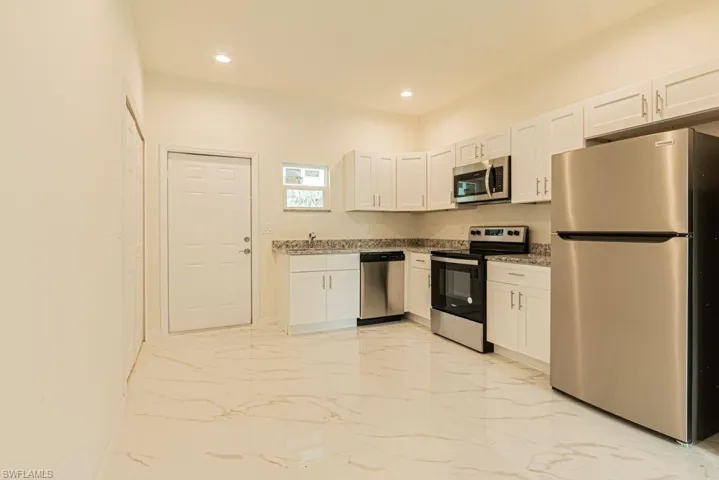 Kitchen with white cabinetry, light stone countertops, appliances with stainless steel finishes, sink, and light tile floors