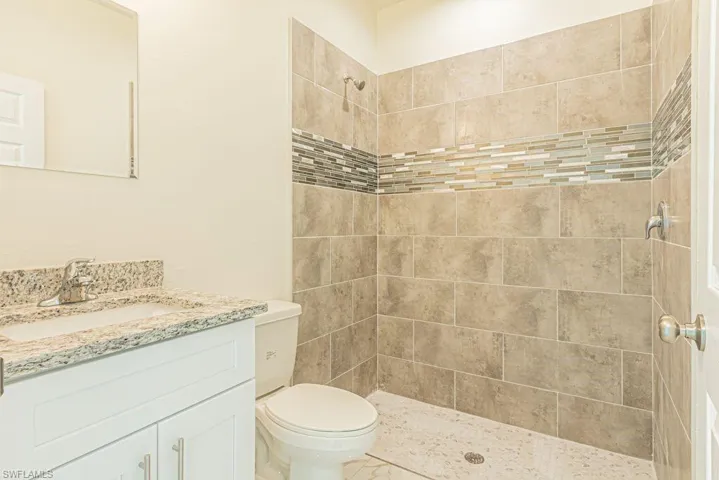 Bathroom with tiled shower, oversized vanity, and toilet