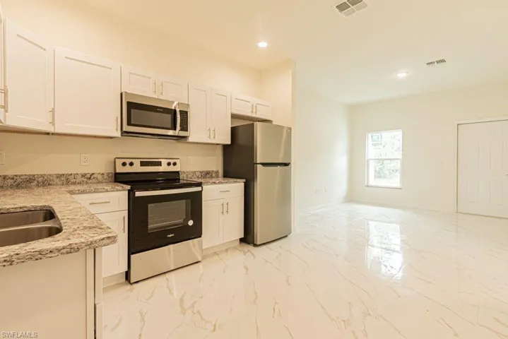 Kitchen featuring light stone countertops, appliances with stainless steel finishes, white cabinets, sink, and light tile floors