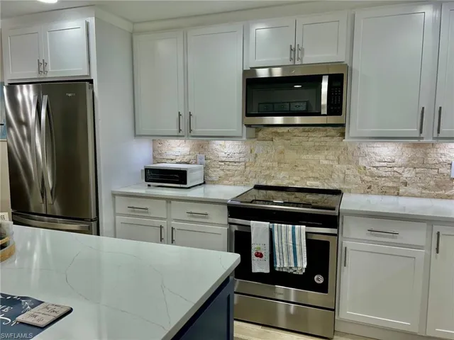 Kitchen featuring appliances with stainless steel finishes, white cabinetry, and light stone countertops