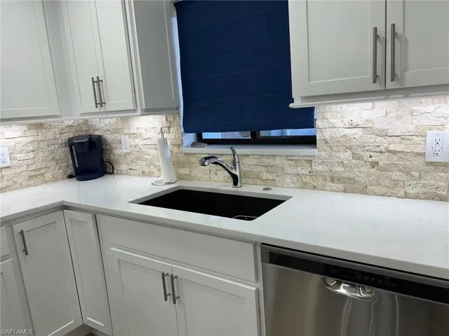 Kitchen featuring decorative backsplash, light stone counters, sink, and stainless steel dishwasher