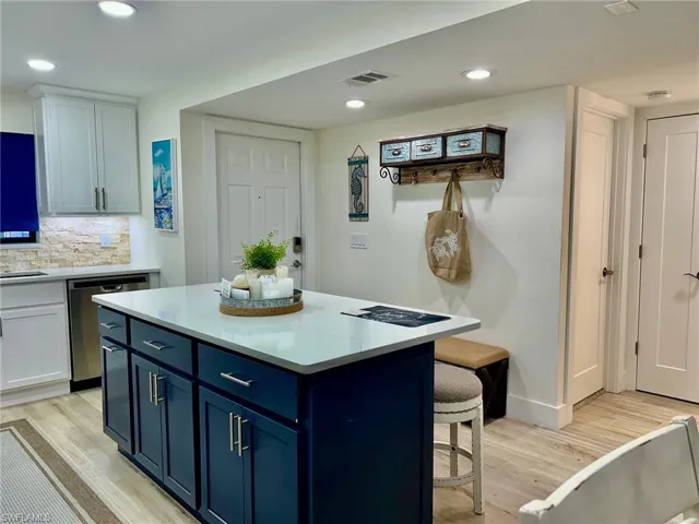 Kitchen with tasteful backsplash, dishwasher, a kitchen island, light wood-type flooring, and white cabinetry