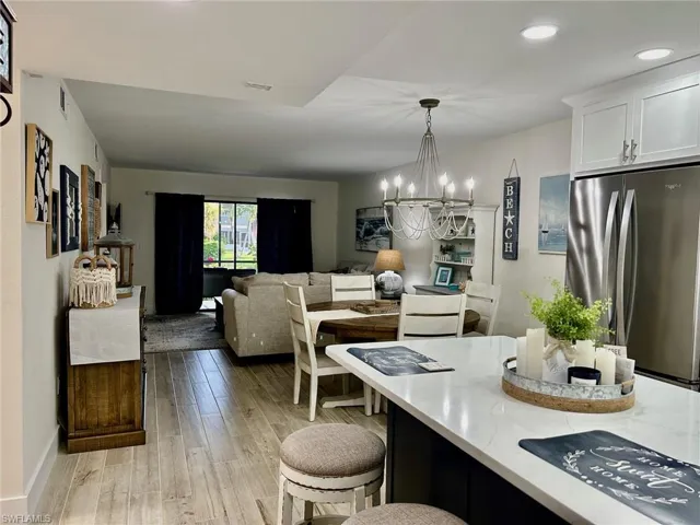 Kitchen with white cabinetry, a chandelier, hanging light fixtures, light hardwood / wood-style floors, and stainless steel refrigerator