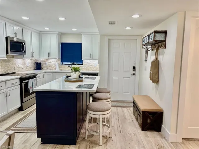 Kitchen with appliances with stainless steel finishes, tasteful backsplash, white cabinets, and light hardwood / wood-style floors