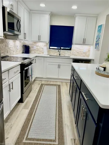 Kitchen with stainless steel appliances, light wood-type flooring, tasteful backsplash, and sink