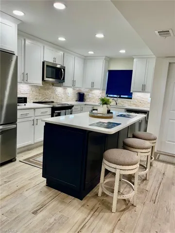 Kitchen with light hardwood / wood-style flooring, white cabinets, tasteful backsplash, and stainless steel appliances
