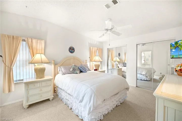 Bedroom with a textured ceiling, two closets, visible vents, ceiling fan, and light colored carpet