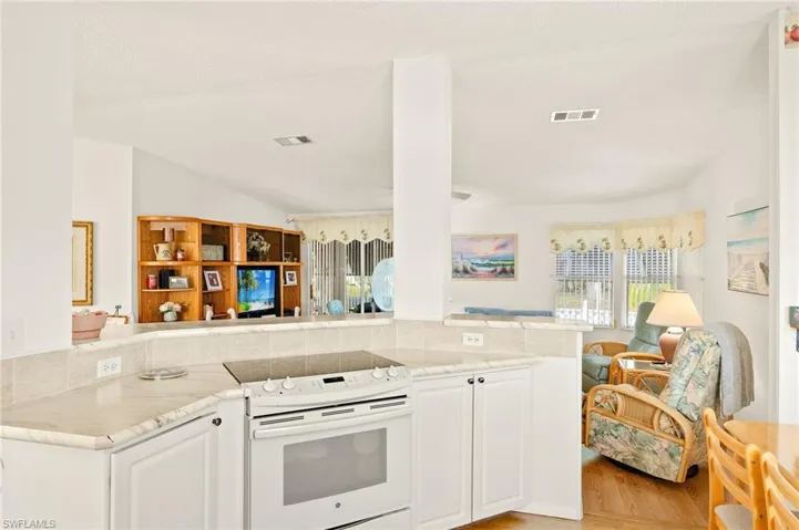 Kitchen featuring white range with electric cooktop, white cabinets, visible vents, light stone counters, and open floor plan