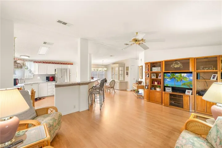 Living room featuring light wood-style flooring, ceiling fan with notable chandelier, and visible vents