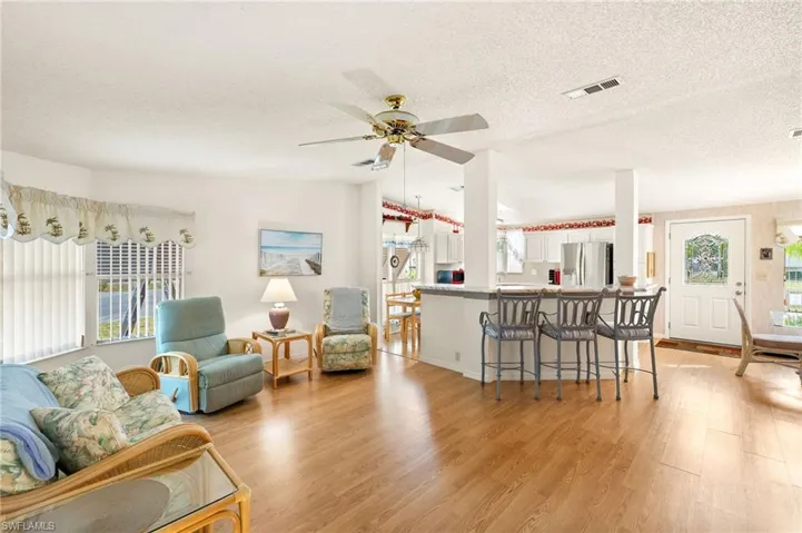 Living room with light wood finished floors, ceiling fan, vaulted ceiling, and visible vents