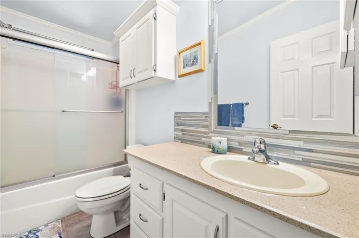 Full bathroom featuring crown molding, vanity, toilet, enclosed tub / shower combo, and decorative backsplash