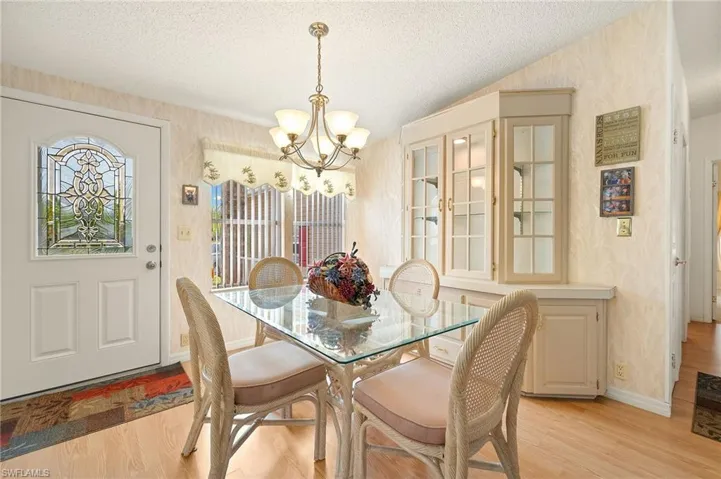Dining area with baseboards, wallpapered walls, an inviting chandelier, light wood-style flooring, and a textured ceiling