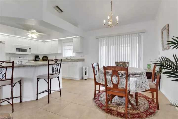 Dining space featuring visible vents, ceiling fan with notable chandelier, lofted ceiling, and light tile patterned floors