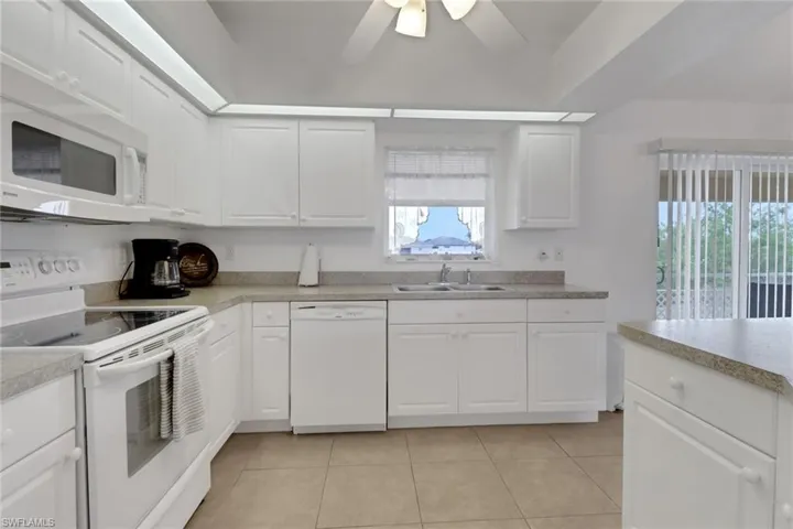 Kitchen with a ceiling fan, a sink, light tile patterned floors, white appliances, and white cabinetry