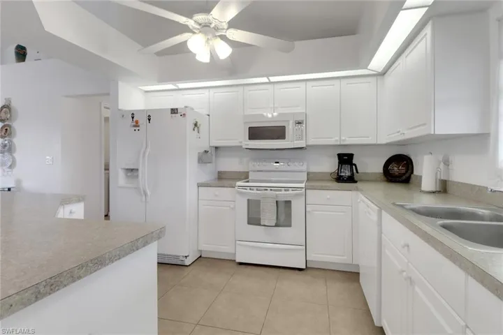 Kitchen featuring white appliances, light tile patterned floors, white cabinetry, and a sink