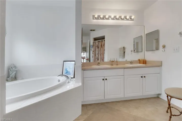 Full bath featuring double vanity, a sink, tile patterned flooring, and a garden tub