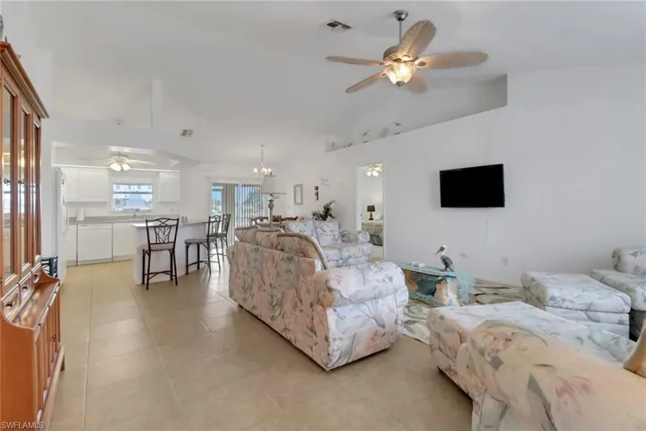 Living room with visible vents, ceiling fan with notable chandelier, light tile patterned floors, and high vaulted ceiling
