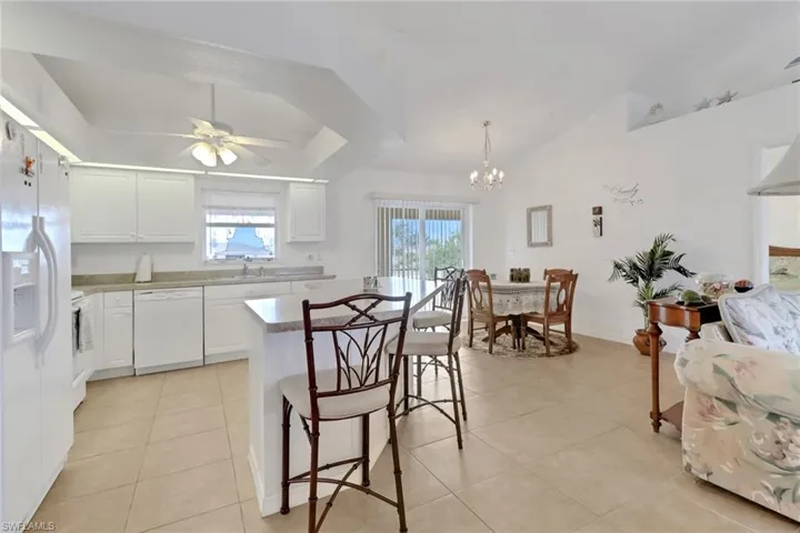 Kitchen with light tile patterned floors, plenty of natural light, a breakfast bar, and white appliances