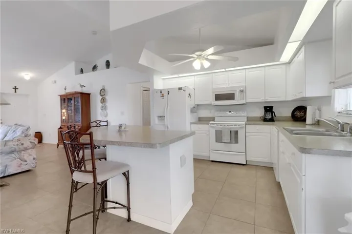Kitchen with light tile patterned flooring, white appliances, ceiling fan, a kitchen bar, and a sink