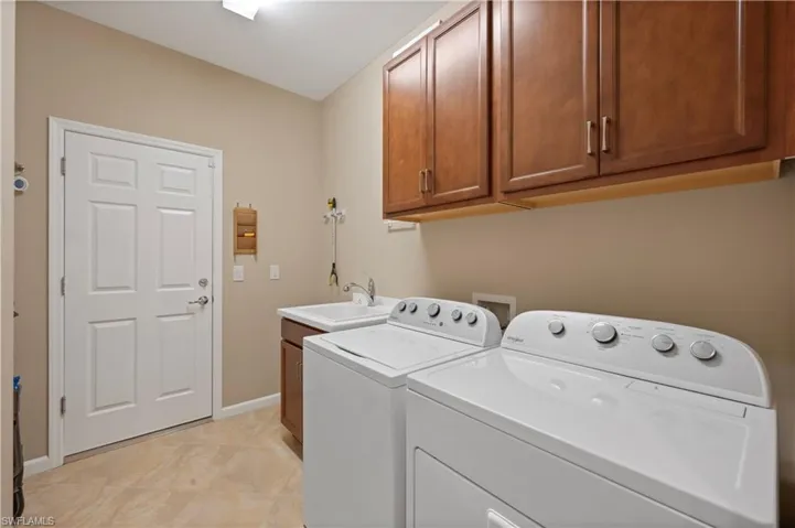 Washroom with washing machine and dryer, washer hookup, light tile floors, sink, and cabinets