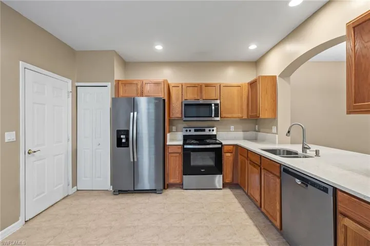 Kitchen with light tile patterned floors, sink, stainless steel appliances, and light stone countertops