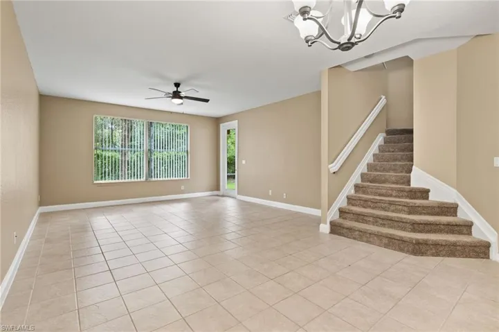 open floor plan with stairs to loft and bedrooms with light tile patterned flooring, ceiling fan with notable chandelier, and a wealth of natural light