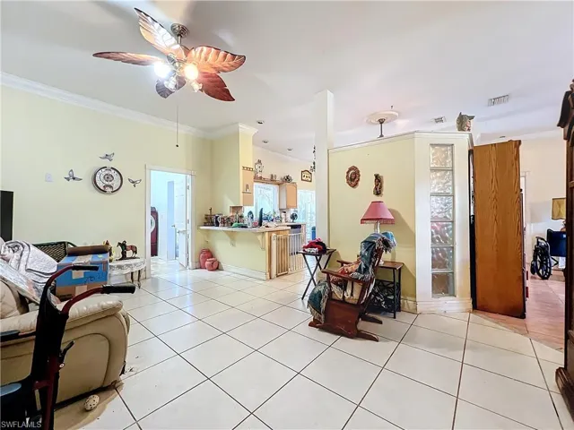 Living area with light tile patterned flooring, baseboards, visible vents, ceiling fan, and ornamental molding