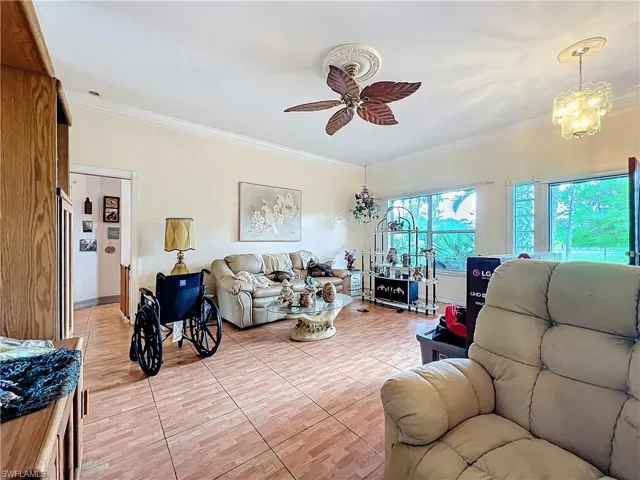 Living room with light tile patterned floors, ornamental molding, and ceiling fan with notable chandelier