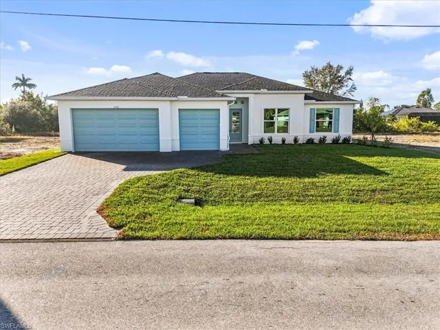 View of front of house with stucco siding, a front yard, decorative driveway, and a garage