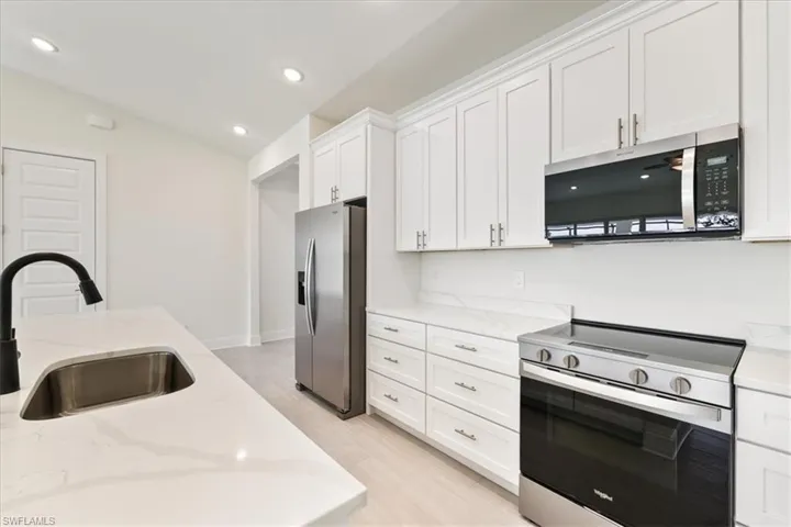 Kitchen featuring appliances with stainless steel finishes, light stone countertops, white cabinetry, recessed lighting, and vaulted ceiling