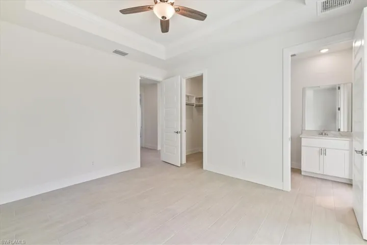 Unfurnished bedroom with a tray ceiling, a walk in closet, ensuite bathroom, ceiling fan, and crown molding