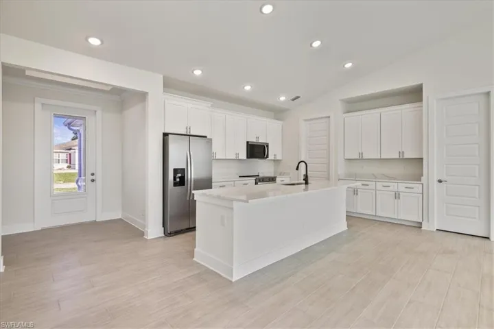 Kitchen with appliances with stainless steel finishes, white cabinetry, a kitchen island with sink, lofted ceiling, and light wood finished floors