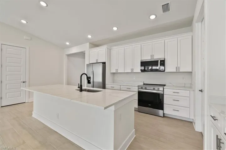 Kitchen featuring stainless steel appliances, a kitchen island with sink, white cabinets, wood tiled floors, and light stone countertops