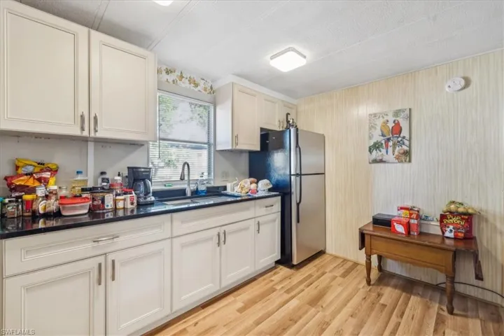 Kitchen with freestanding refrigerator, light wood-style floors, cream cabinets, dark stone counters, and a textured ceiling