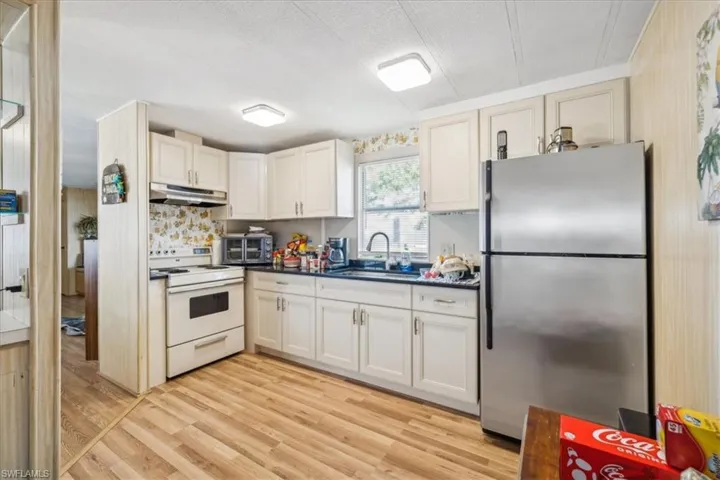 Kitchen featuring freestanding refrigerator, white electric range oven, dark countertops, light wood-style floors, and cream cabinetry
