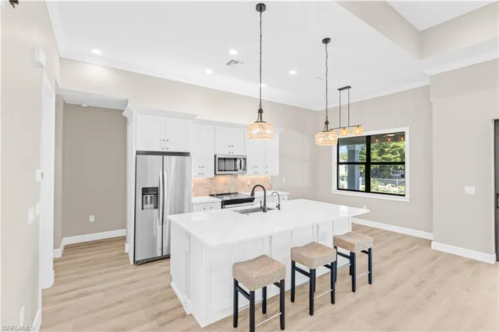 Kitchen featuring stainless steel appliances, a breakfast bar, white cabinetry, light stone counters, and pendant lighting