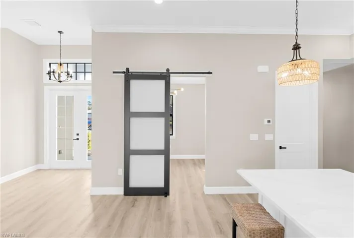 Unfurnished dining area featuring a barn door, a chandelier, light wood finished floors, french doors, and crown molding