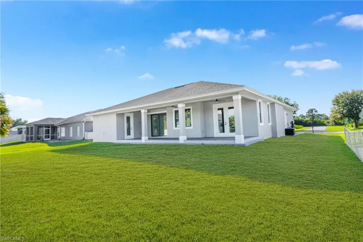 Rear view of house featuring a lawn, ceiling fan, and stucco siding