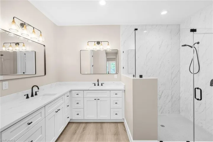Full bathroom featuring a marble finish shower, double vanity, light wood-style flooring, and recessed lighting