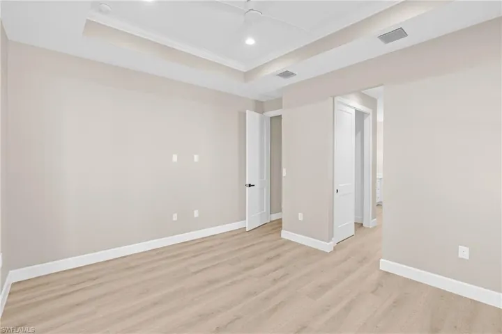 Empty room featuring a raised ceiling, recessed lighting, ornamental molding, light wood-type flooring, and a ceiling fan