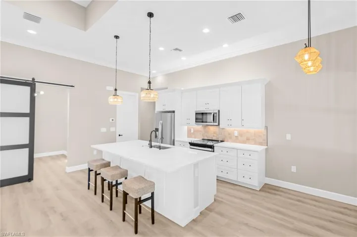 Kitchen with a barn door, white cabinetry, a kitchen island with sink, decorative backsplash, and a breakfast bar area