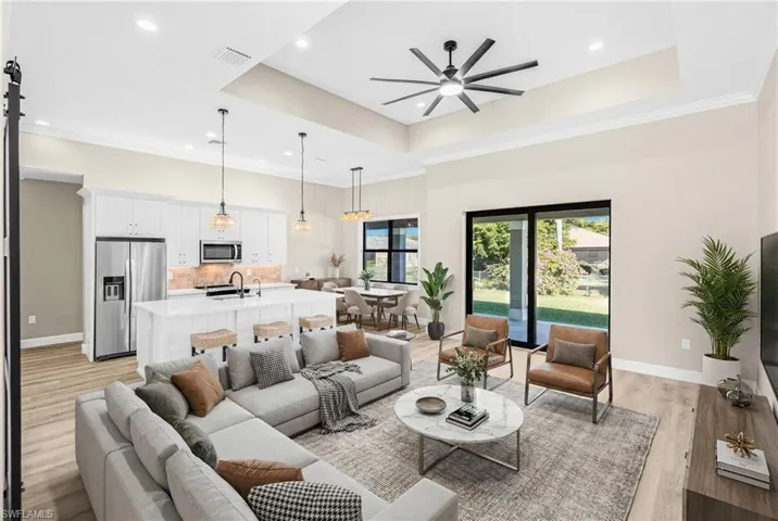 Living room with ceiling fan, a barn door, light wood finished floors, ornamental molding, and recessed lighting