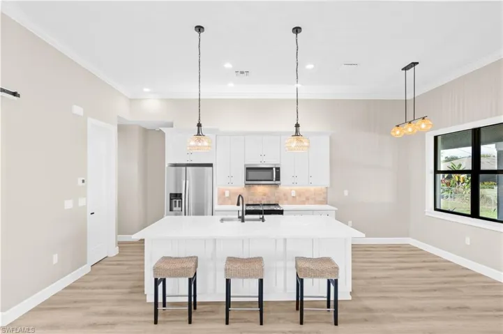 Kitchen with ornamental molding, white cabinets, decorative backsplash, a kitchen island with sink, and appliances with stainless steel finishes